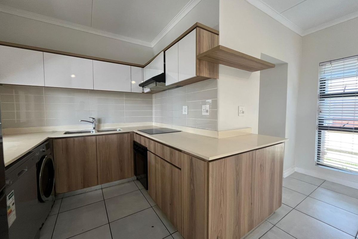 Modern kitchen featuring wood-grain cabinetry, stone countertops, integrated electric hob, extractor fan, and neutral tiled flooring in a clean, contemporary layout.