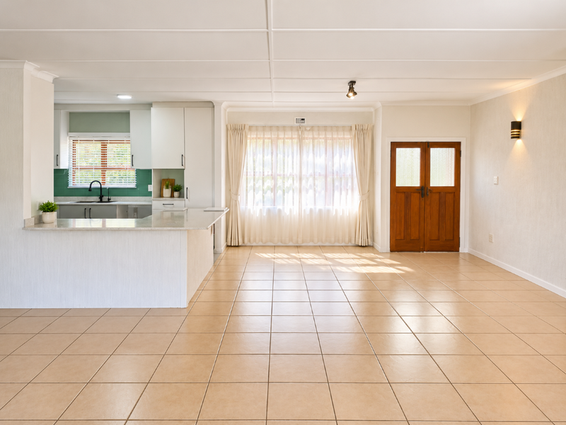 Spacious open-plan living area featuring tiled flooring, a modern kitchen with stone countertops, and a classic double wooden entrance door.
