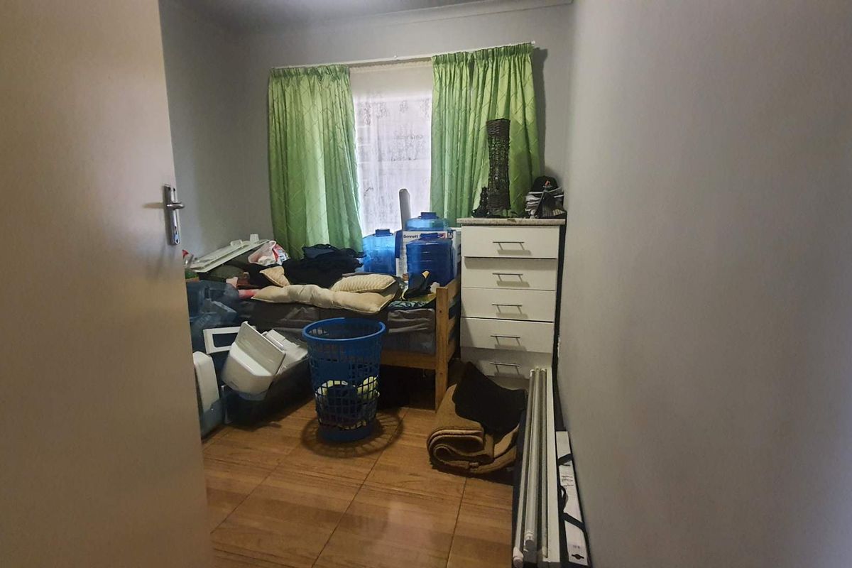 A compact bedroom featuring tiled flooring and a window with curtain tracks, offering a functional space for a single bed or home office setup.