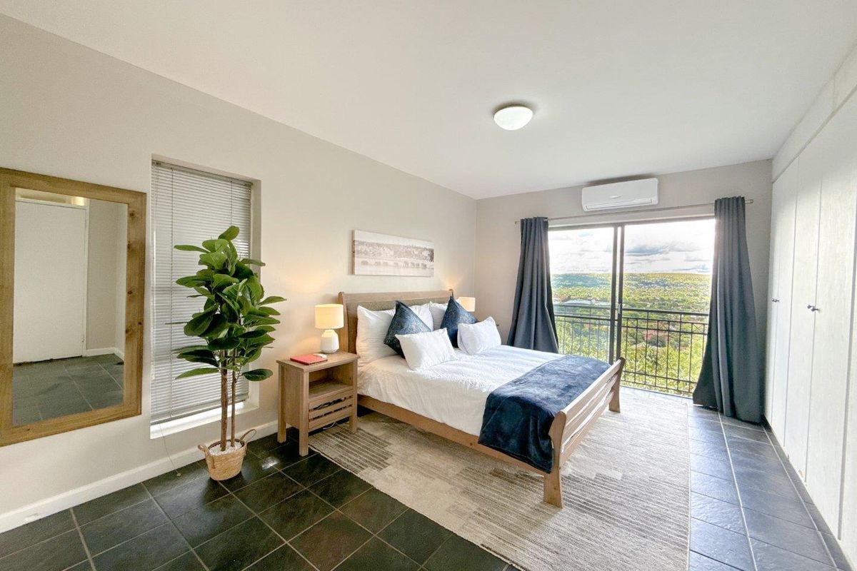 A well-lit bedroom featuring dark tiled flooring, a wall-mounted air conditioning unit, and sliding glass doors that open to a scenic balcony view.