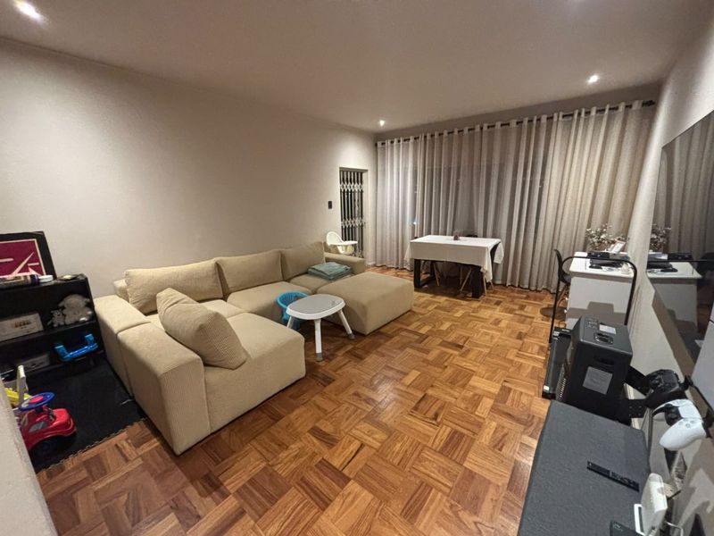 Spacious living room featuring warm parquet flooring, recessed downlighting, and a secure entrance gate, offering a comfortable and well-maintained living space.