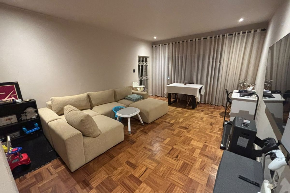 Spacious living room featuring warm parquet flooring, recessed downlighting, and a secure entrance gate, offering a comfortable and well-maintained living space.