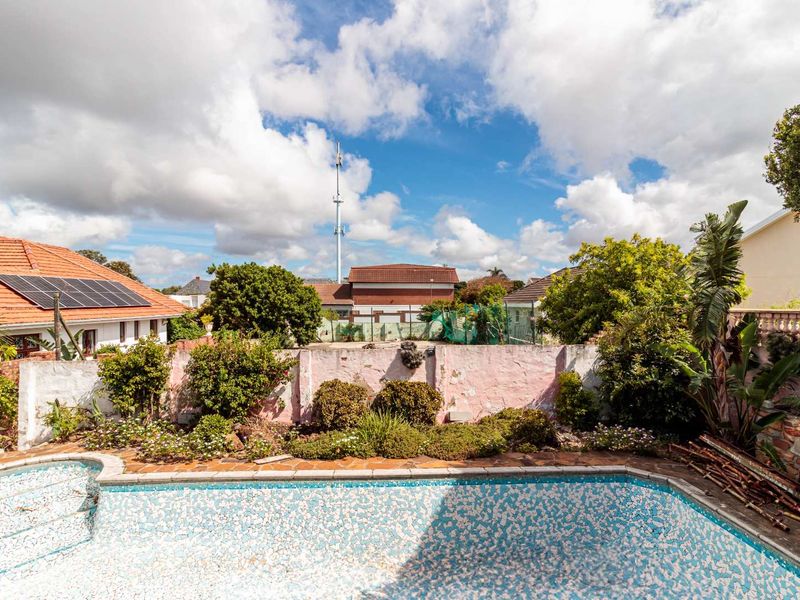 Outdoor pool area featuring a tiled swimming pool, established garden beds, and a perimeter boundary wall with visible wear.