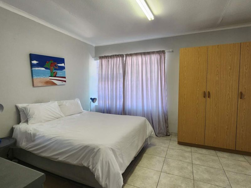 A functional bedroom featuring neutral wall tones, tiled flooring, and a large built-in wooden wardrobe providing ample storage space.