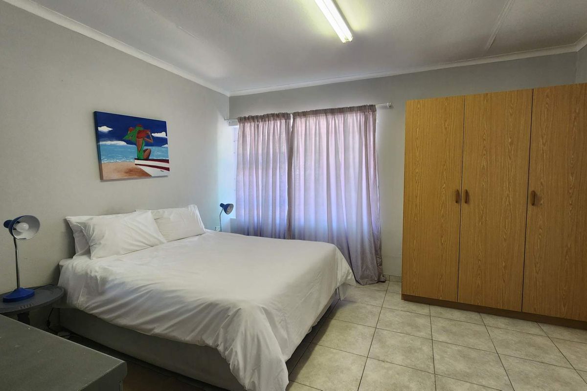 A functional bedroom featuring neutral wall tones, tiled flooring, and a large built-in wooden wardrobe providing ample storage space.