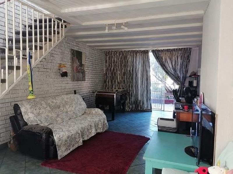 A living room featuring exposed brick walls, tiled flooring, and an open staircase leading to the upper level, with direct access to an outdoor area.