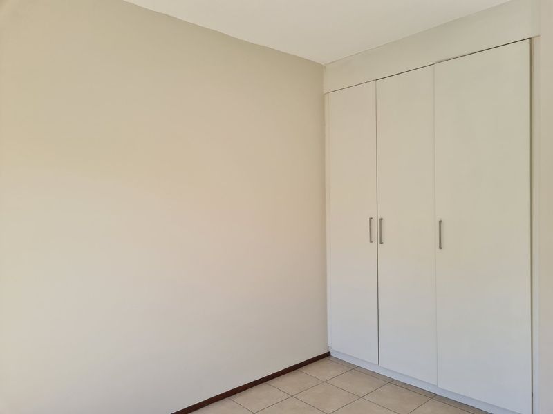 A clean, empty bedroom featuring neutral walls, tiled flooring, and ample built-in cupboard storage.