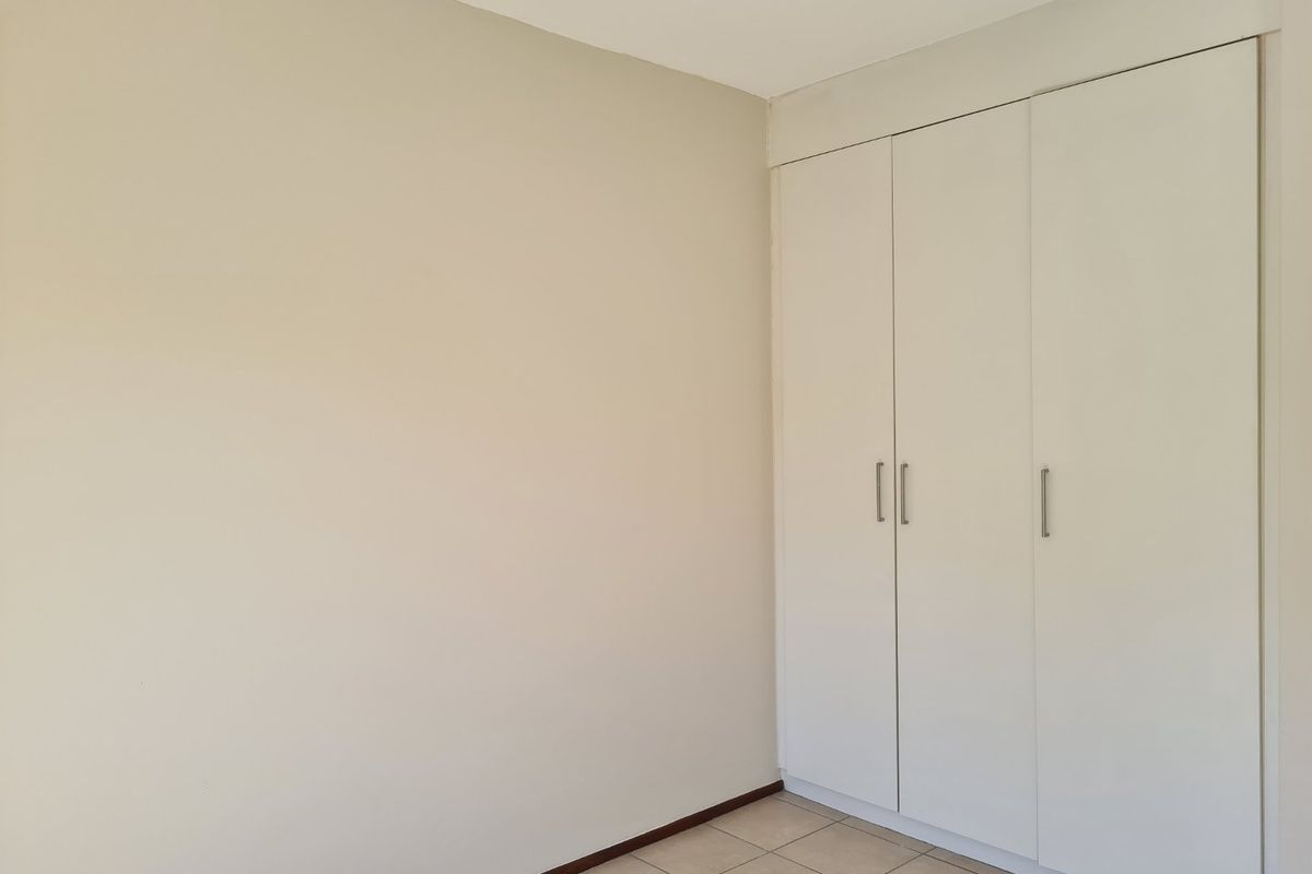 A clean, empty bedroom featuring neutral walls, tiled flooring, and ample built-in cupboard storage.