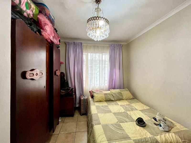 A compact bedroom featuring tiled flooring, a decorative crystal chandelier, and a window fitted with security bars.
