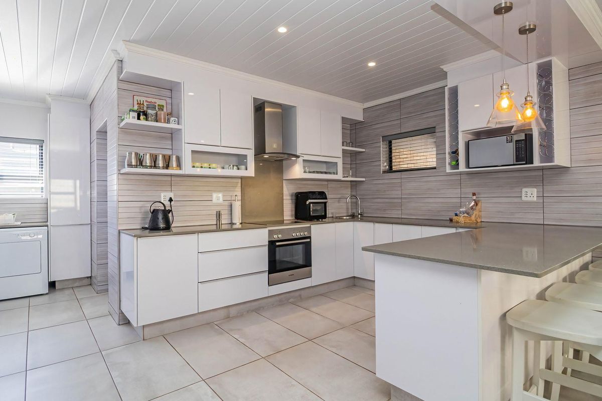Modern kitchen featuring sleek white cabinetry, stone countertops, integrated stainless steel appliances, and stylish pendant lighting with a clean, contemporary finish.