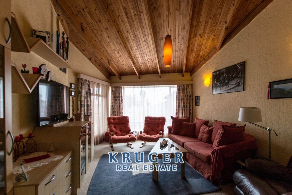 A cozy living room featuring a high vaulted timber-paneled ceiling, textured walls, and large windows that provide ample natural light.