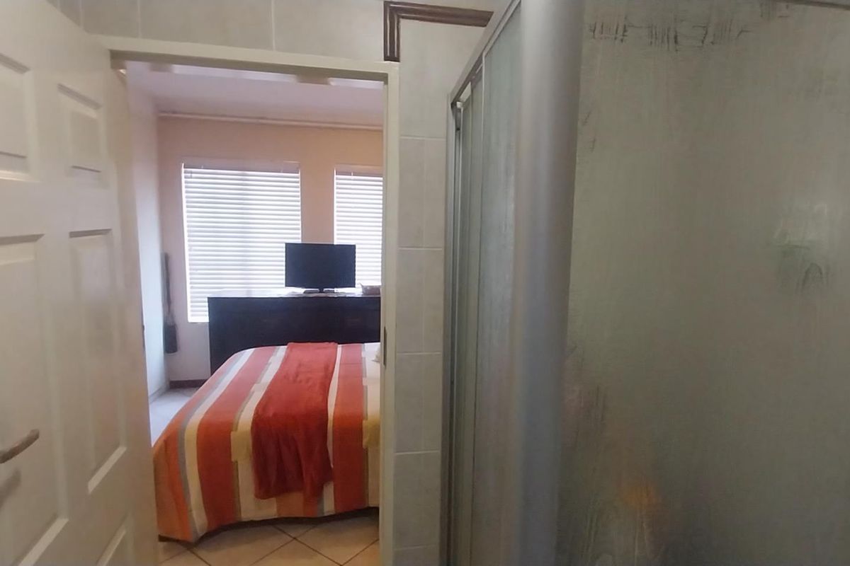 A view from a tiled bathroom looking into a bedroom, featuring a built-in shower enclosure with frosted glass doors.