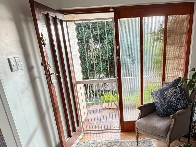 Entrance area featuring a timber-framed glass door with ribbed glass sidelights and a security gate, providing a bright and welcoming transition to the home.