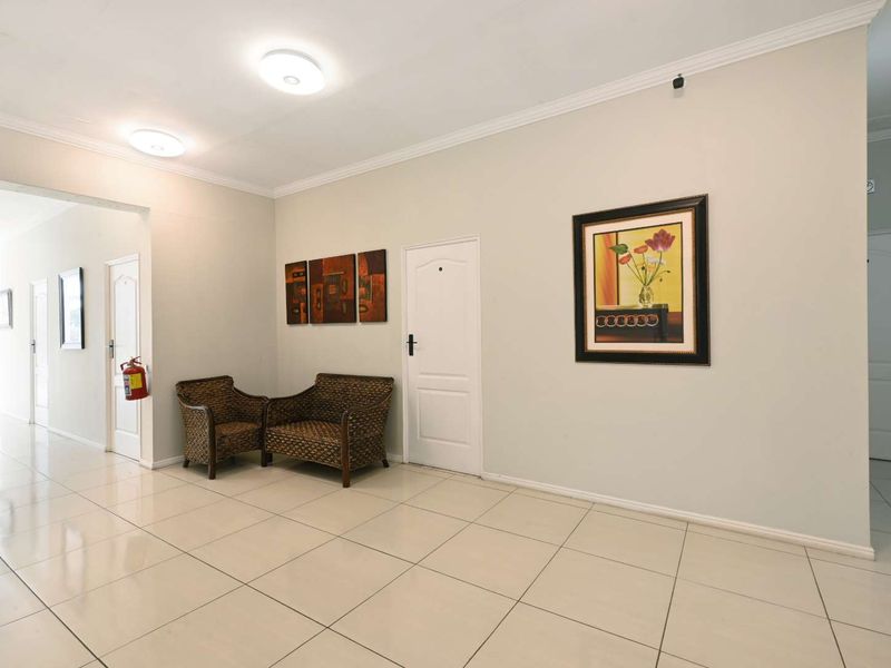 A spacious, well-lit hallway featuring neutral tiled flooring, coving, and multiple internal access points, providing a clean and functional transition space.