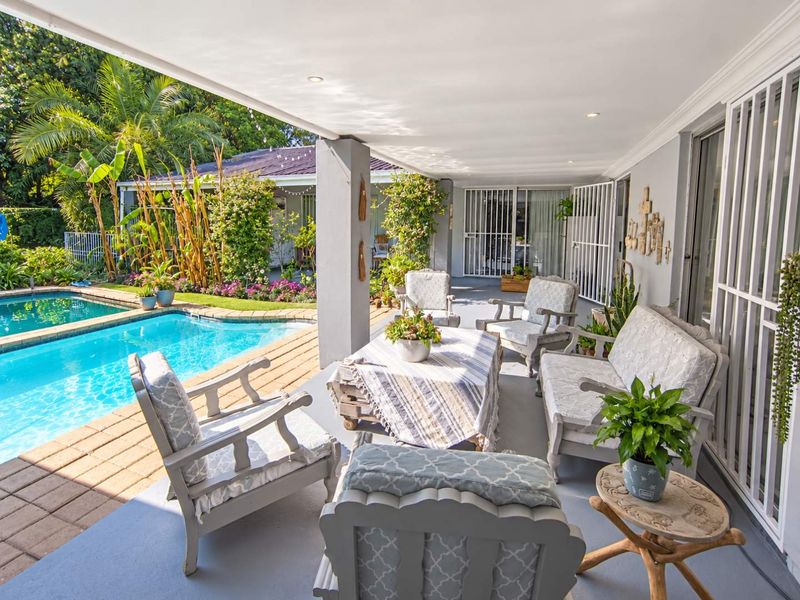 A spacious covered patio overlooking a swimming pool and landscaped garden, featuring recessed lighting and secure access to the main dwelling.
