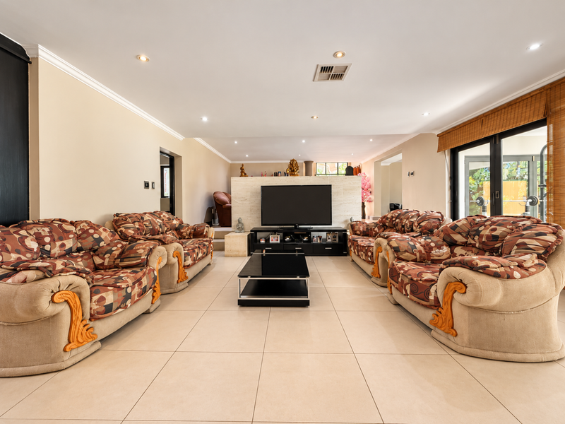 Spacious living room featuring large format floor tiles, a central stone feature wall, recessed downlighting, and sliding glass doors leading to the exterior.