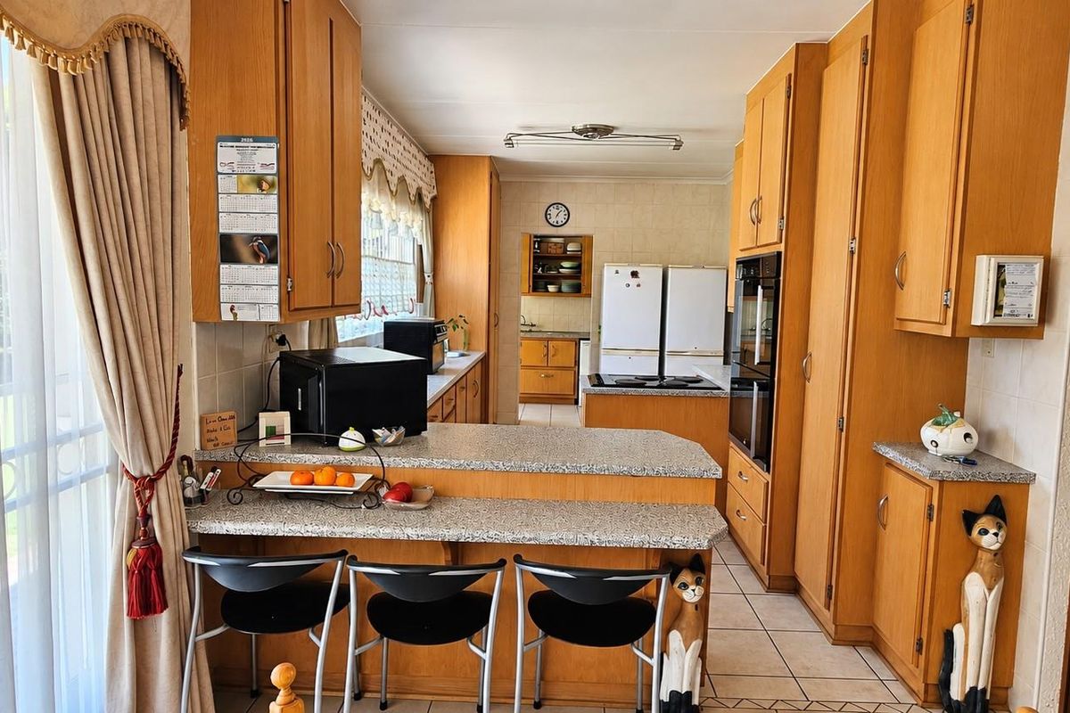 A functional kitchen featuring extensive wooden cabinetry, granite countertops, a breakfast bar, and built-in appliances, with direct access to the outdoor area.