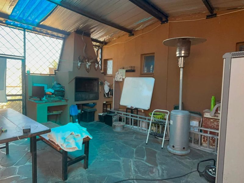 Covered outdoor patio area featuring a built-in braai, stone flooring, and a corrugated metal roof structure.