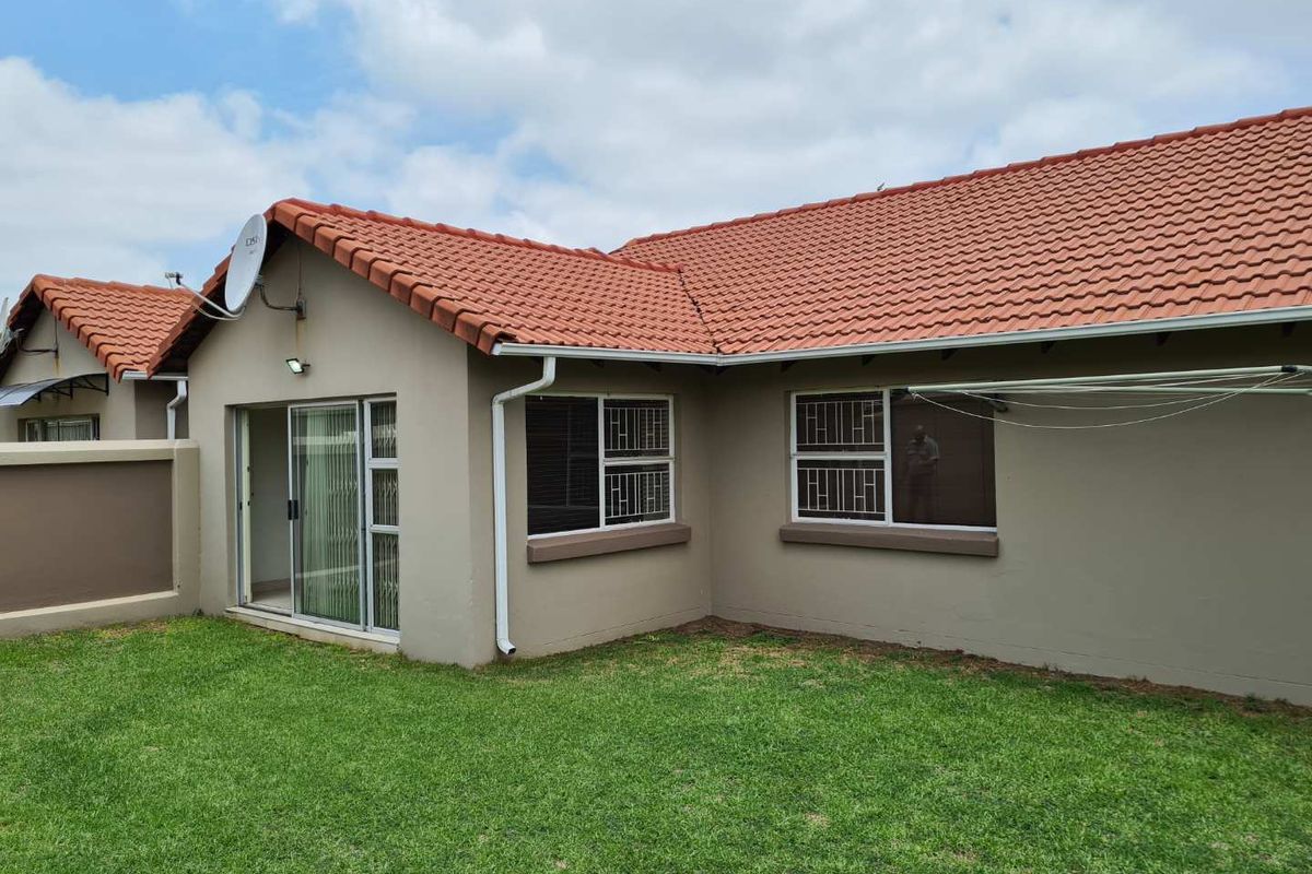 Rear view of the townhouse featuring a tiled roof, sliding glass doors, security bars on windows, and a well-maintained lawn area.