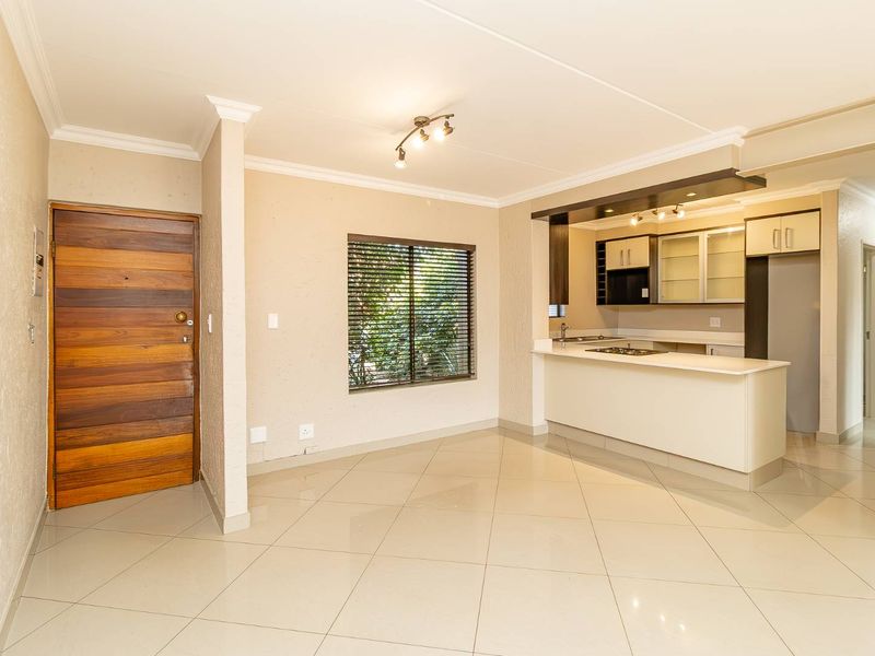 Open-plan living and kitchen area featuring tiled flooring, modern cabinetry, a breakfast island with integrated hob, and a solid timber entrance door.