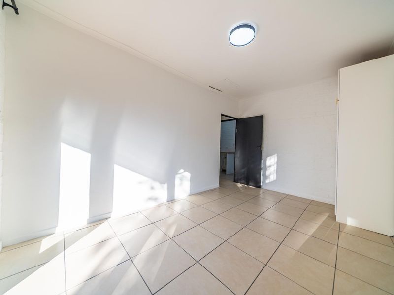 A bright, empty bedroom featuring neutral tiled flooring and a built-in cupboard, offering a clean canvas for personalization.