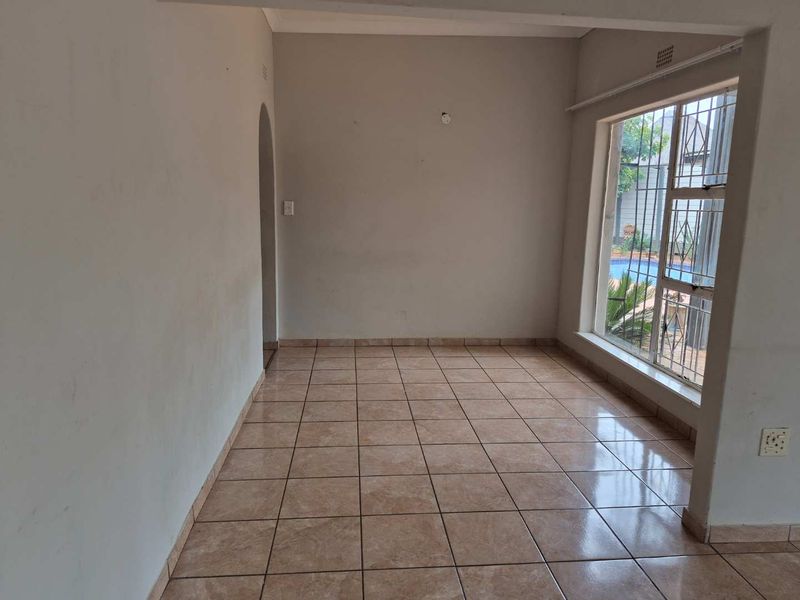 An empty living area featuring neutral ceramic floor tiles, a large window with security bars, and an arched entryway.