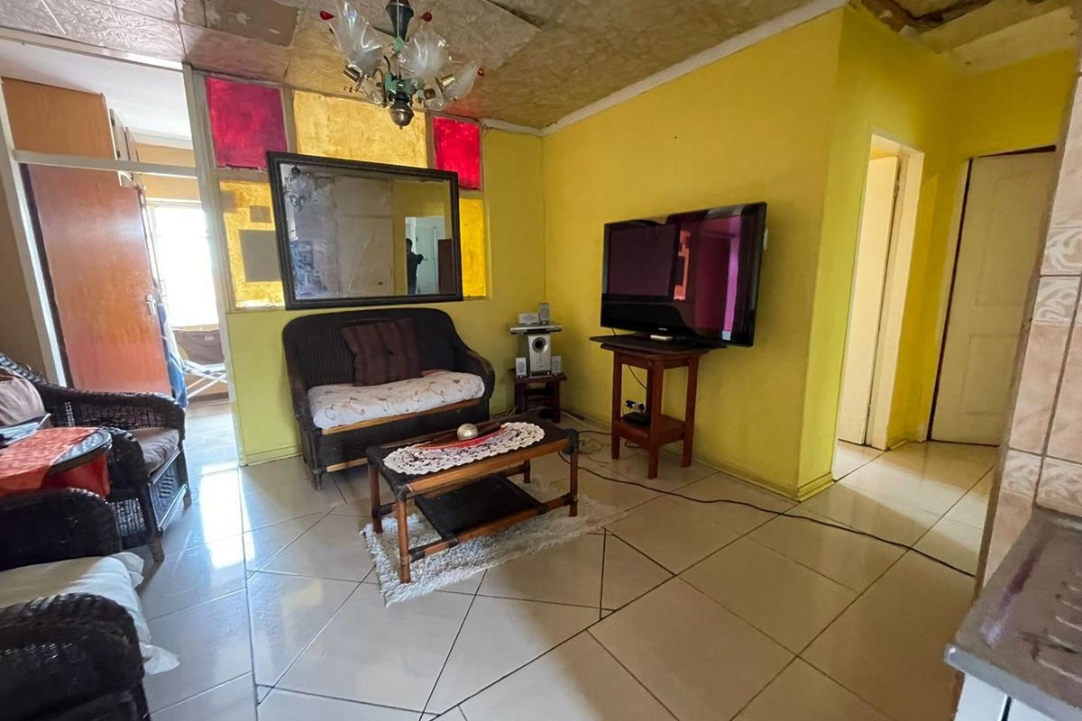 A living room area featuring tiled flooring, yellow walls, and decorative stained glass accents, requiring significant cosmetic updates and ceiling repairs.