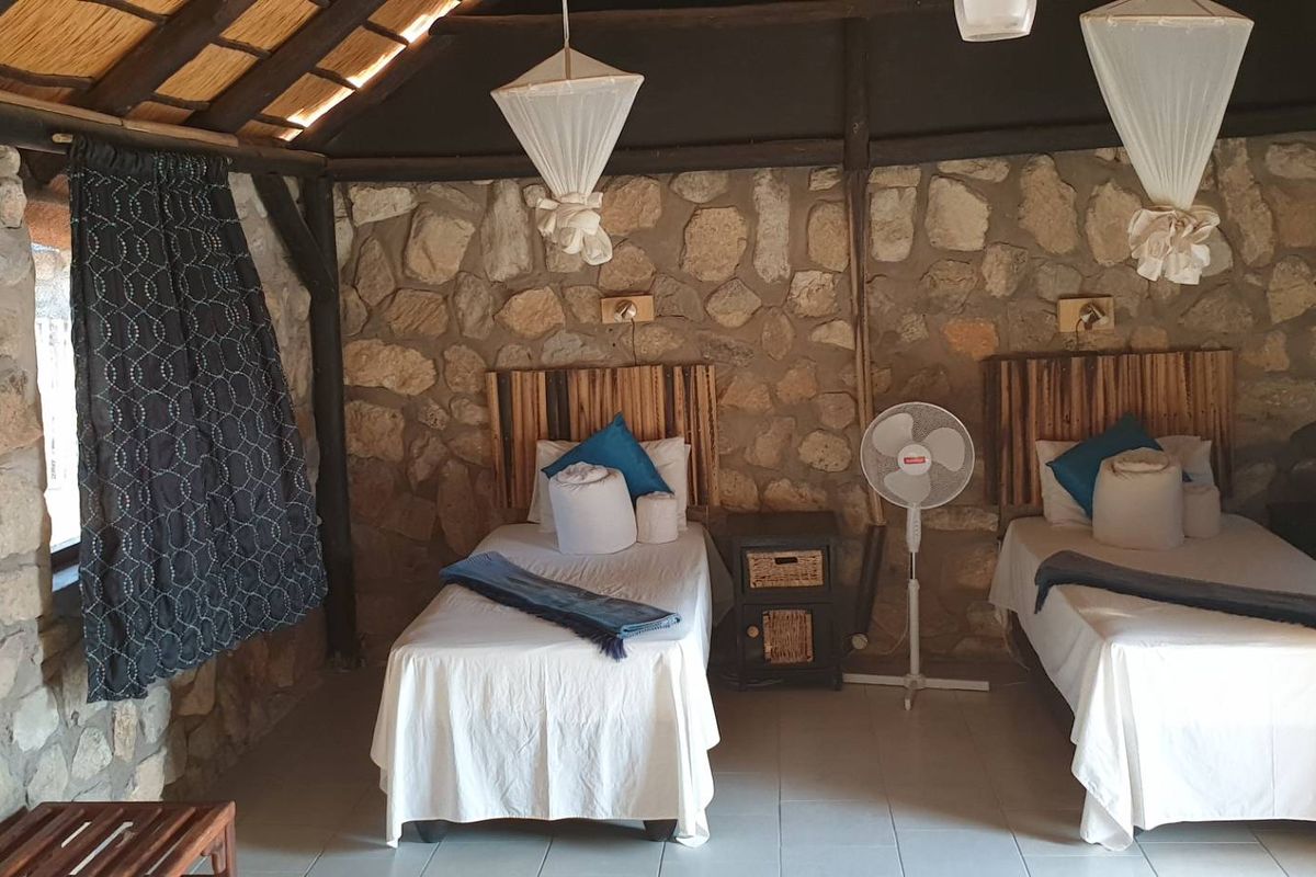 A rustic lodge bedroom featuring exposed stone walls, a traditional thatched roof, and tiled flooring, creating a natural and authentic bushveld atmosphere.