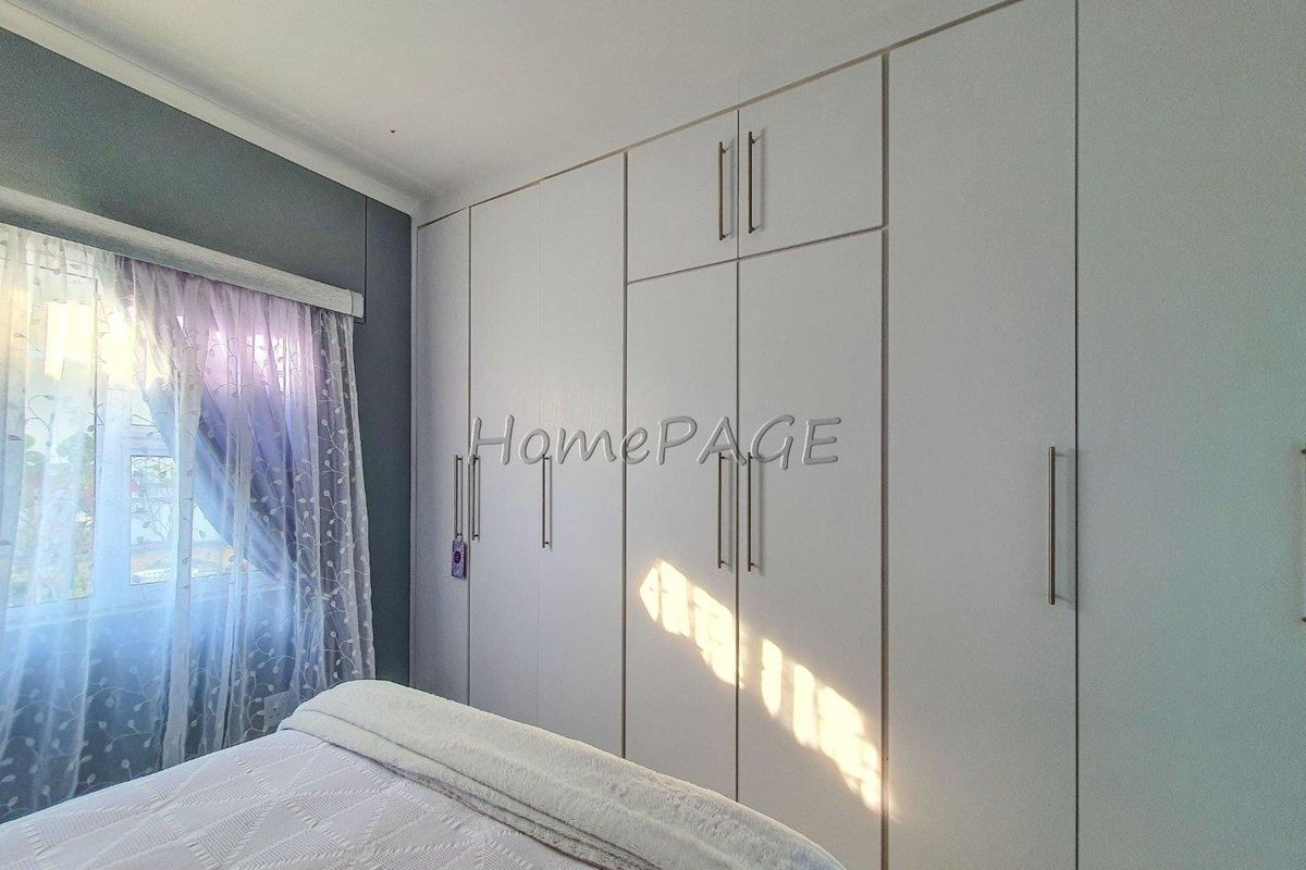 A bedroom featuring floor-to-ceiling built-in wardrobes with modern handles and a window with sheer curtains.