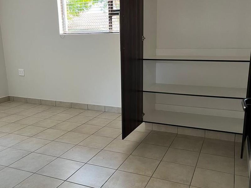 A clean, empty bedroom featuring neutral tiled flooring, a built-in wardrobe, and a window with fitted blinds, offering a bright and versatile living space.