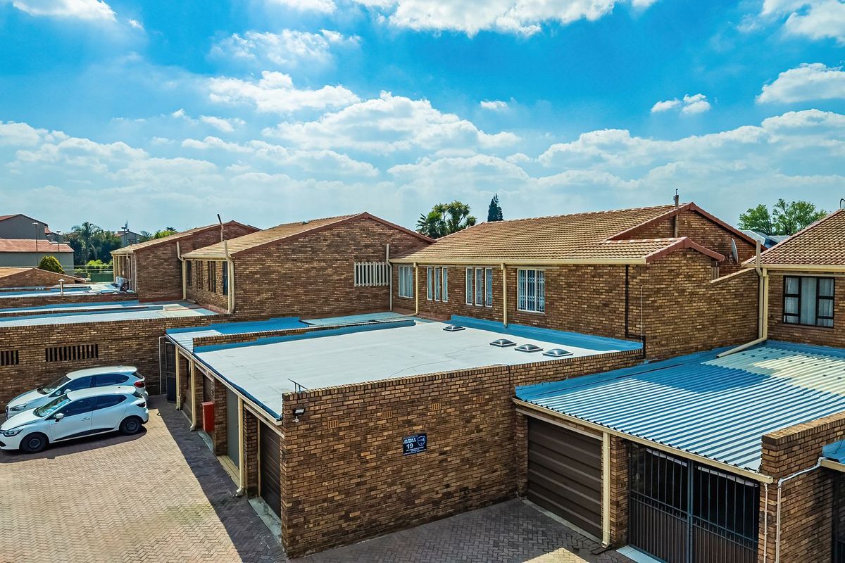 Aerial view of a townhouse complex featuring face brick construction, tiled and metal roofing, paved driveways, and multiple garage units.