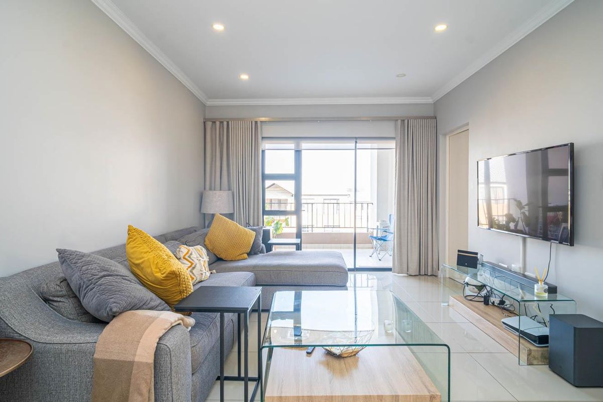 A bright and modern living room featuring tiled flooring, recessed downlighting, and direct access to a private balcony through sliding glass doors.