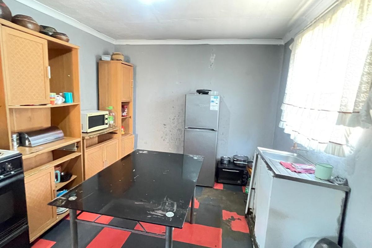 A dated kitchen area featuring basic cabinetry, a stainless steel sink, and worn flooring, requiring significant cosmetic updates and renovation.