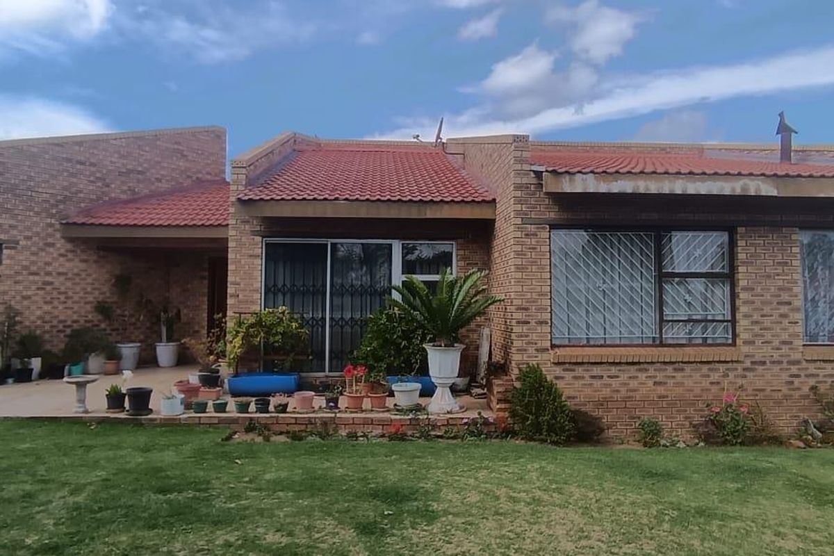 Rear view of a single-story brick house featuring a tiled roof, concrete patio area, and established lawn.