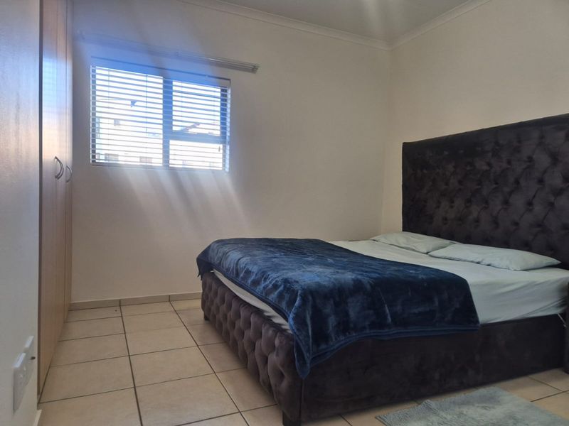 A bedroom featuring tiled flooring, built-in cupboards, and a window fitted with venetian blinds, offering a functional and neutral living space.