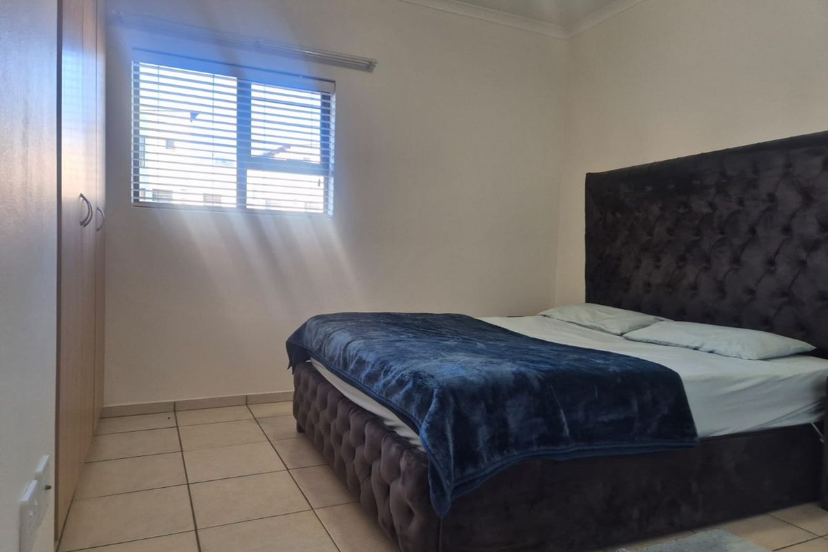 A bedroom featuring tiled flooring, built-in cupboards, and a window fitted with venetian blinds, offering a functional and neutral living space.