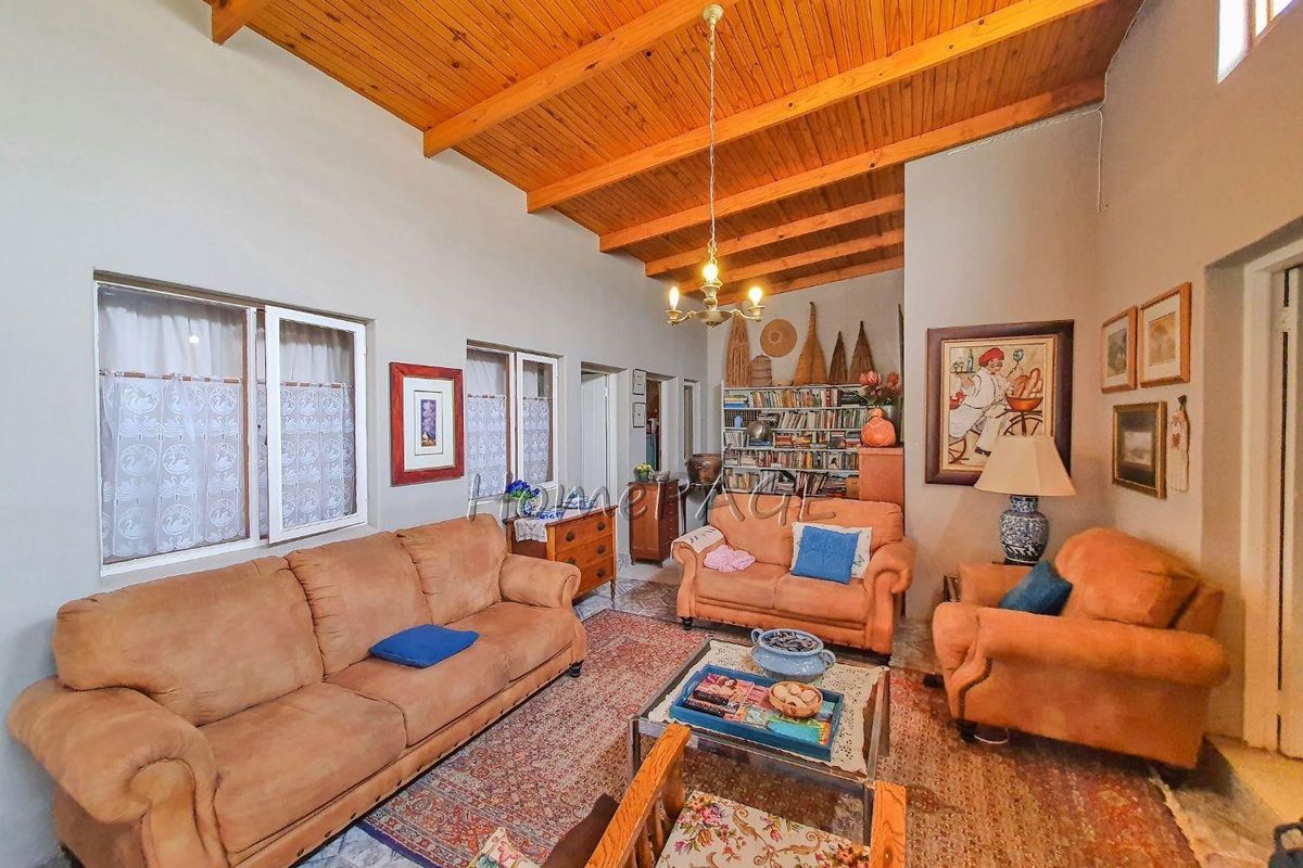 Spacious living room featuring a high vaulted timber-beamed ceiling, tiled flooring, and multiple windows providing natural light.