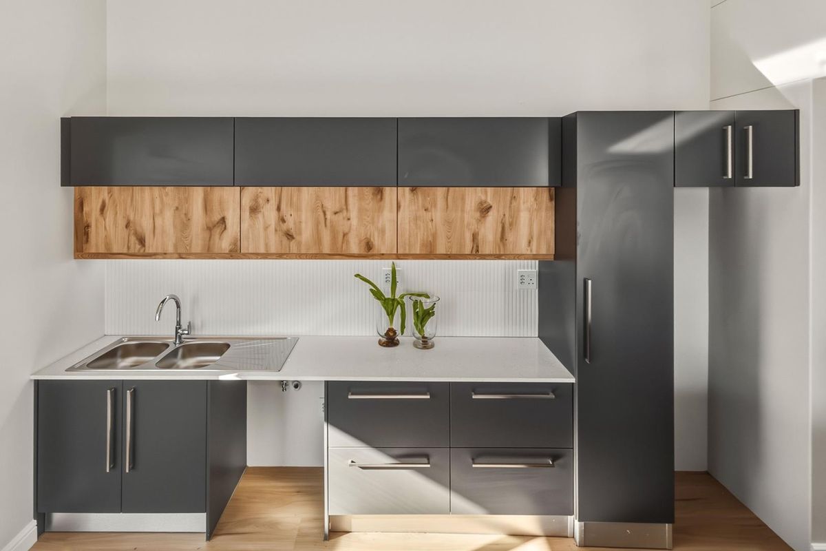 Modern kitchen featuring sleek dark grey cabinetry, natural wood accents, a double stainless steel sink, and a clean white countertop.