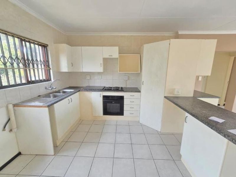 A functional kitchen featuring built-in cabinetry, laminate countertops, a gas hob, and an integrated oven, with tiled flooring and security bars on the window.