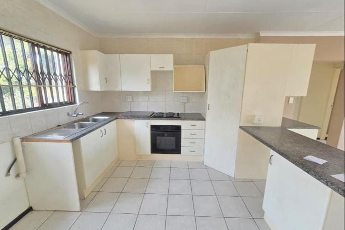 A functional kitchen featuring built-in cabinetry, laminate countertops, a gas hob, and an integrated oven, with tiled flooring and security bars on the window.
