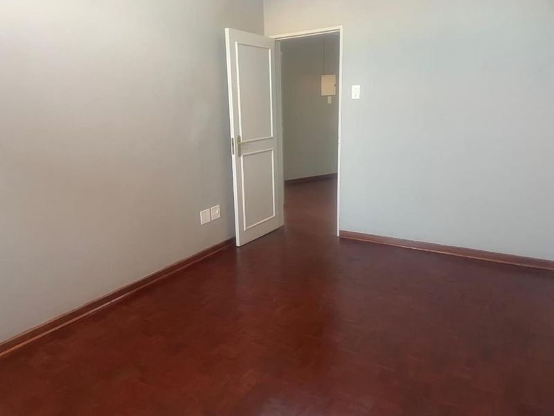 An empty bedroom featuring dark parquet flooring, neutral wall paint, and a classic internal door leading to an adjacent space.