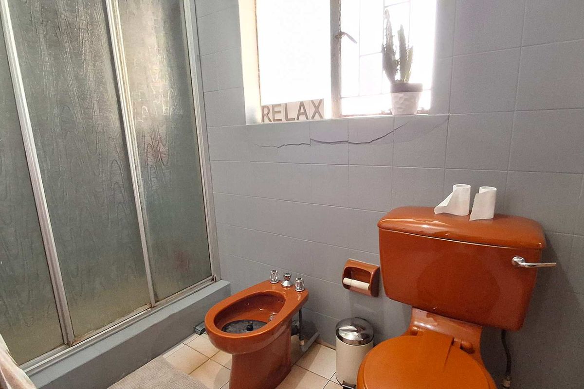 A dated bathroom featuring a shower enclosure, bidet, and toilet, with visible cracking in the wall tiling requiring maintenance.