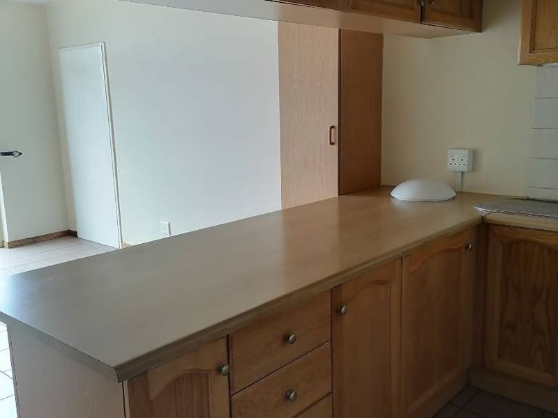 A functional kitchen area featuring wooden cabinetry, laminate countertops, and tiled flooring, offering a clean and neutral space ready for updates.
