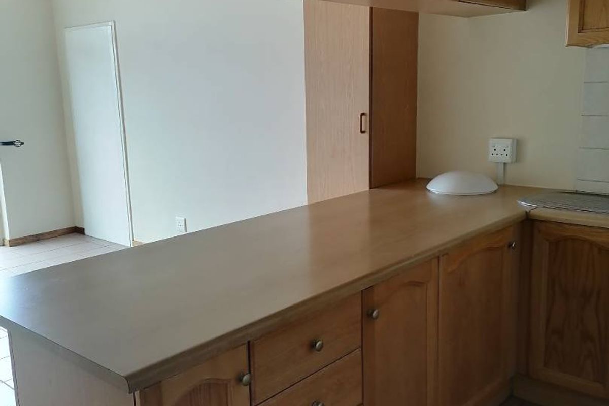 A functional kitchen area featuring wooden cabinetry, laminate countertops, and tiled flooring, offering a clean and neutral space ready for updates.