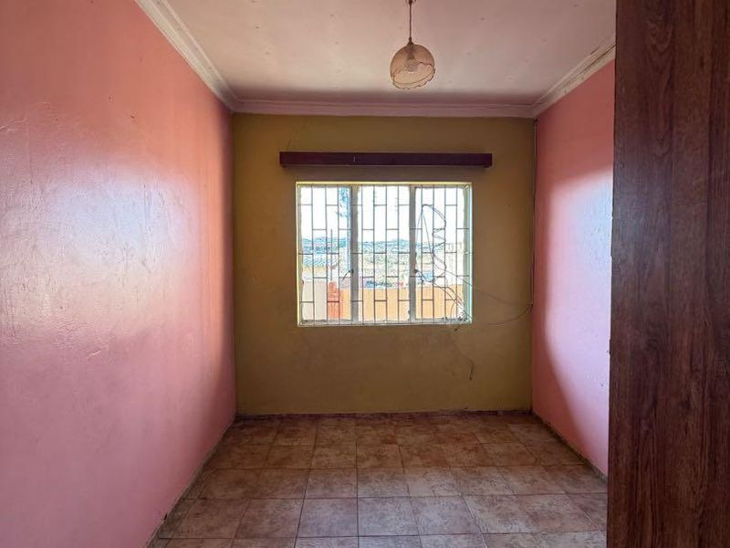An empty bedroom featuring tiled flooring, security bars on the window, and coving, requiring cosmetic updates to the walls and ceiling.