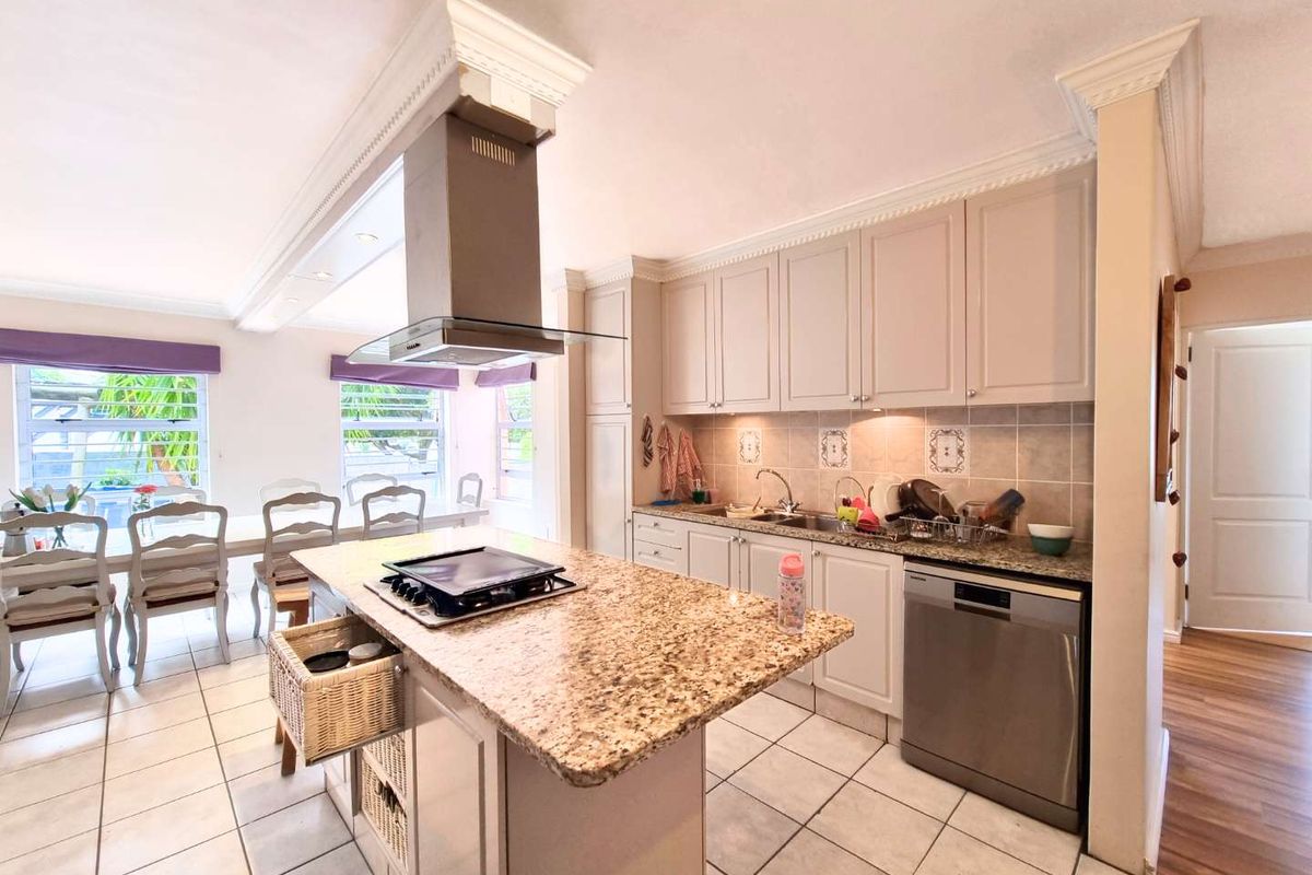A well-appointed kitchen featuring a central island with a built-in hob, stainless steel extractor fan, granite countertops, and ample cabinetry.