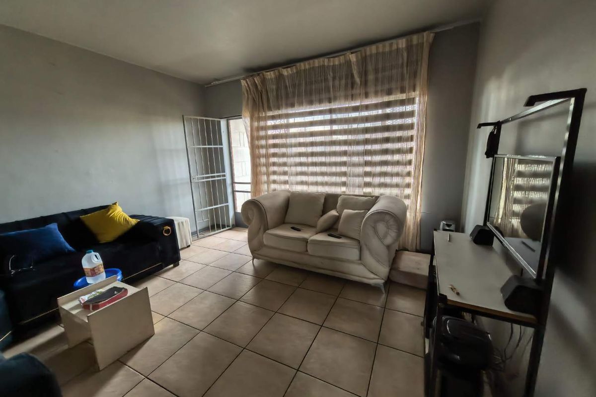 A living room featuring tiled flooring, a large window with fitted blinds, and a security gate leading to an outdoor area.