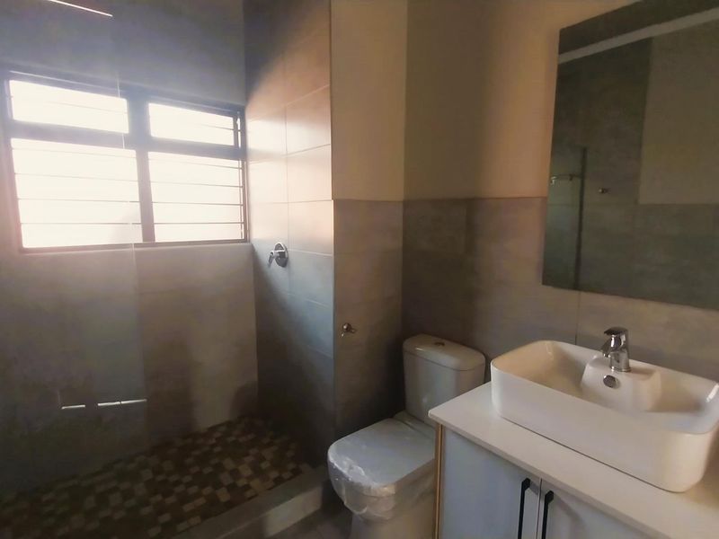 Modern bathroom featuring a vessel sink on a vanity cabinet, a toilet, and a walk-in shower with tiled flooring and neutral wall tiles.