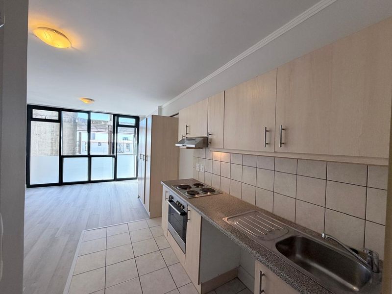 An open-plan kitchen and living area featuring light wood cabinetry, built-in appliances, tiled splashback, and large glass doors leading to an outdoor space.
