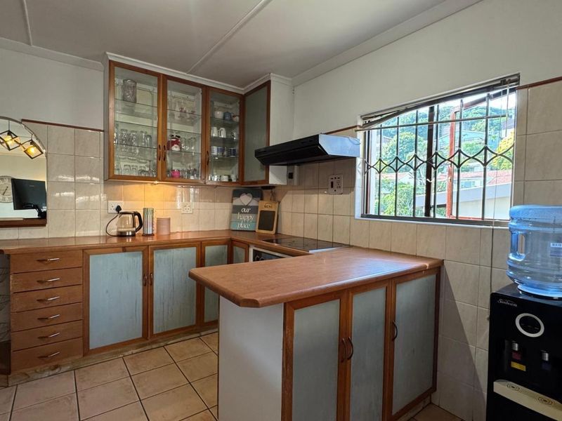 A functional kitchen featuring wooden cabinetry, laminate countertops, tiled splashbacks, and an integrated extractor fan, offering a classic layout with potential for modern updates.